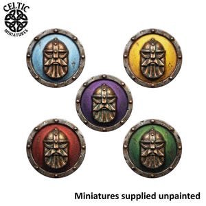 May include: Five circular miniature shields featuring a central bronze-coloured relief of a bearded warrior in a helmet. Each shield has a distinct coloured background: light blue, yellow, purple, red, and green, with a metallic silver-toned rim.