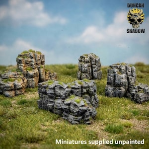 May include: A set of grey, textured rock formations with patches of green moss, arranged on a grassy field. The text "DUNCAN SHADOW" appears in the top right corner with a skull logo, and "Miniatures supplied unpainted" is at the bottom.