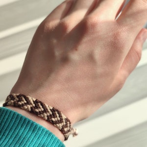 Puede incluir: Un brazalete de amistad marrón y beige con un patrón de chevron.