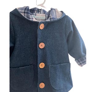 May include: A blue denim jacket with a plaid lining and brown buttons. The jacket has a hood and two pockets.