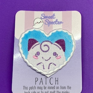 May include: A blue and purple heart-shaped iron-on patch featuring a cartoon ghost with a happy expression. The patch is packaged on a white card with the text "Sweet Specter" and "PATCH" printed on it. The card also includes instructions for ironing the patch on from the back side to avoid melting the minky.