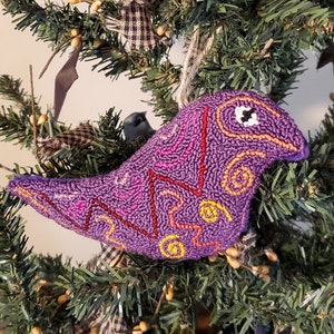 May include: Purple and yellow bird ornament with a whimsical design, hanging on a green Christmas tree.