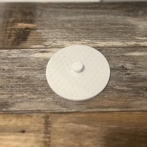 May include: White round lid with a small knob on top. The lid is made of a smooth, textured material.