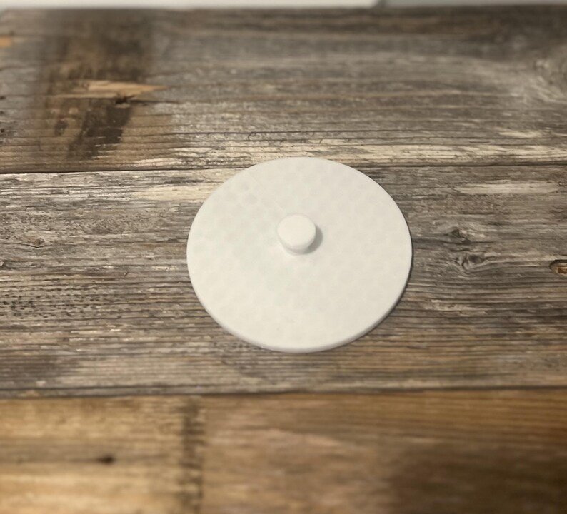 May include: White round lid with a small knob on top. The lid is made of a smooth, textured material.