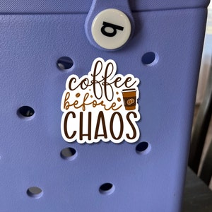 Puede incluir: Una pegatina blanca con texto marrón que dice "coffee before chaos" y una imagen de dibujos animados de una taza de café. La pegatina está sobre un fondo morado claro.