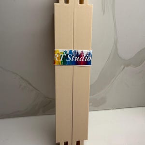Può includere: Un oggetto beige stampato in 3D con forma rettangolare e più fessure nella parte superiore e inferiore. Una fascia colorata con la scritta "RT Studio" avvolge il centro dell'oggetto. L'oggetto sembra essere uno strumento o un espositore.