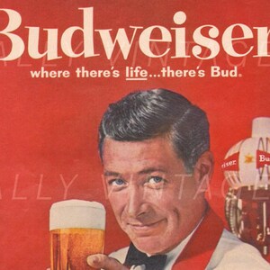 Puede incluir: Un anuncio vintage de cerveza Budweiser con un hombre con camisa blanca y corbata de mo&ntilde;o roja sosteniendo un vaso de cerveza. El anuncio incluye el texto "Budweiser" y "where there's life...there's Bud."