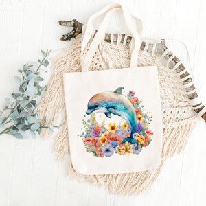 May include: A white canvas tote bag with a colorful watercolor illustration of a dolphin jumping out of a bouquet of flowers. The flowers are in shades of pink, yellow, orange, and purple.