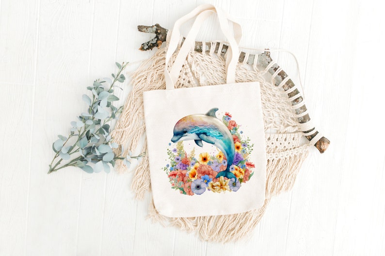 May include: A white canvas tote bag with a colorful watercolor illustration of a dolphin jumping out of a bouquet of flowers. The flowers are in shades of pink, yellow, orange, and purple.