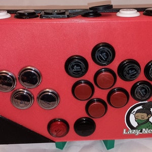 May include: A red arcade cabinet with black and silver buttons, red and black buttons, and a black and white sticker with the text "Lazy Nerds".