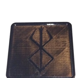 Pu&ograve; includere: Un sottobicchiere quadrato nero con un design in rilievo nero stampato in 3D del simbolo "S" della serie anime Berserk.