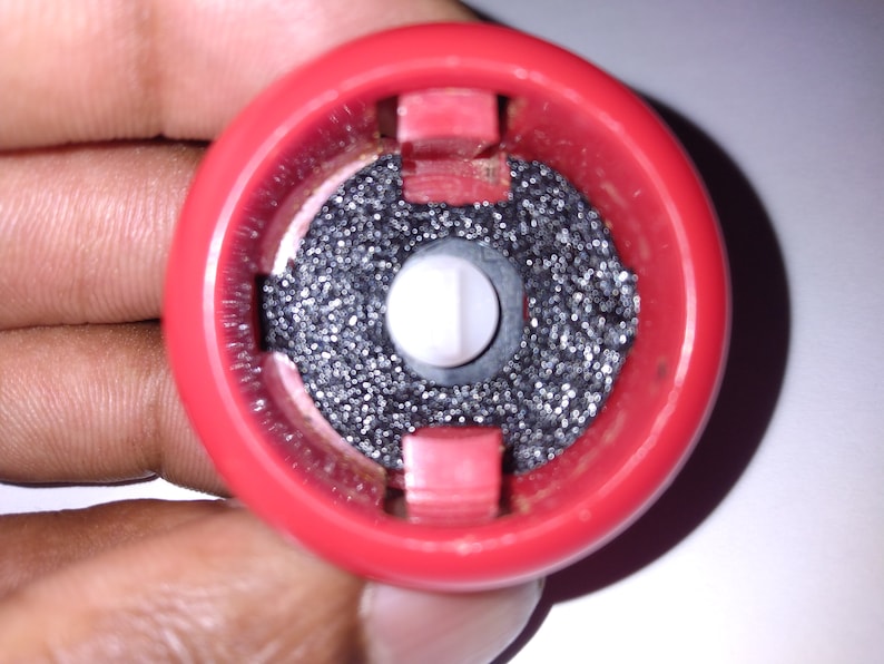 Puede incluir: Primer plano de una tapa de botella de pl&aacute;stico roja con un filtro negro y un bot&oacute;n blanco en el centro.