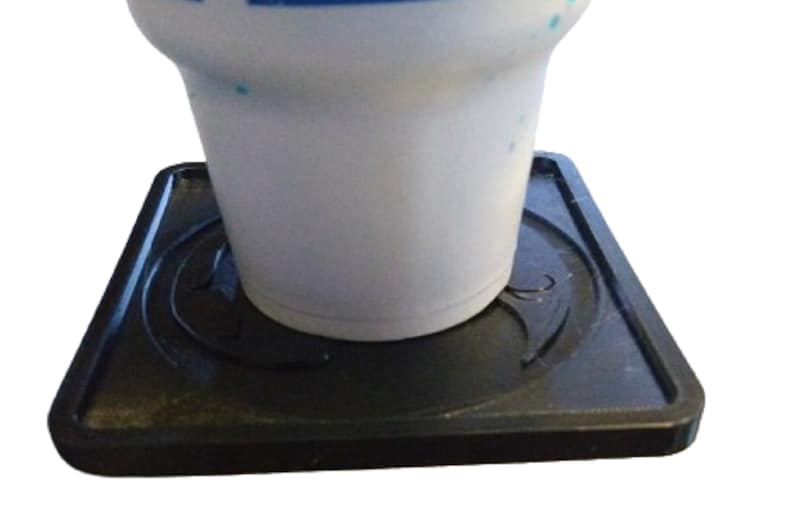 Pu&ograve; includere: Un sottobicchiere quadrato nero con un design rialzato. Il sottobicchiere &egrave; realizzato in un materiale simile alla gomma e ha una superficie liscia. Una tazza in ceramica bianca &egrave; appoggiata sul sottobicchiere.