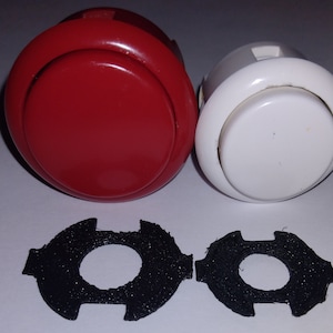 Può includere: Due pulsanti rotondi per arcade, uno rosso e uno bianco, con anelli in plastica nera attorno al pulsante. Due anelli in plastica nera con un foro al centro.