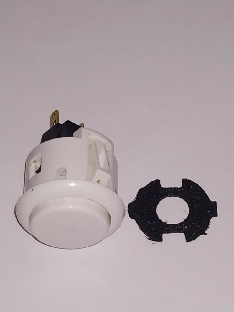 Puede incluir: Bot&oacute;n de arcade blanco con un interruptor negro y dorado y un anillo de montaje de pl&aacute;stico negro.