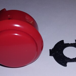 Puede incluir: Un bot&oacute;n de arcade rojo con un anillo de pl&aacute;stico negro. El bot&oacute;n se utiliza para jugar.