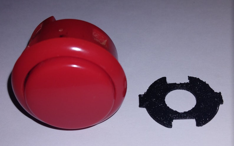 Puede incluir: Un bot&oacute;n de arcade rojo con un anillo de pl&aacute;stico negro. El bot&oacute;n se utiliza para jugar.