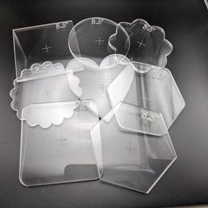 May include: Set of eight clear plastic stencils, each with a different shape, including a heart, a flower, a square, and a hexagon. Each stencil is labeled with "8.5" inches.