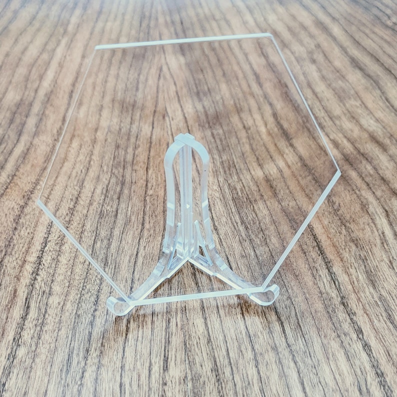 May include: A clear acrylic display stand with a hexagonal base and a three-pronged support.
