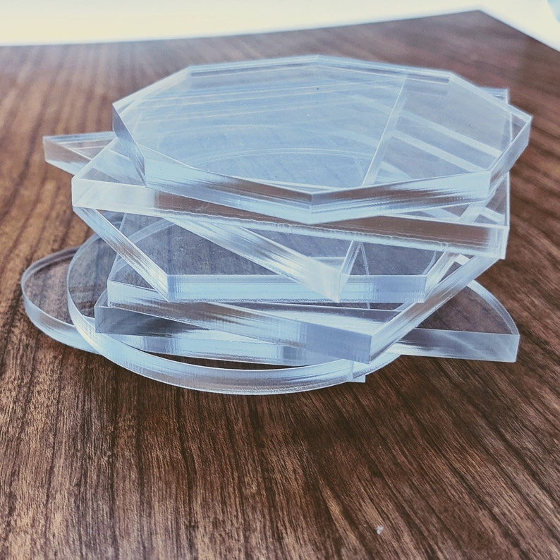 May include: A stack of clear acrylic coasters in various geometric shapes, including a circle, a square, and a hexagon.