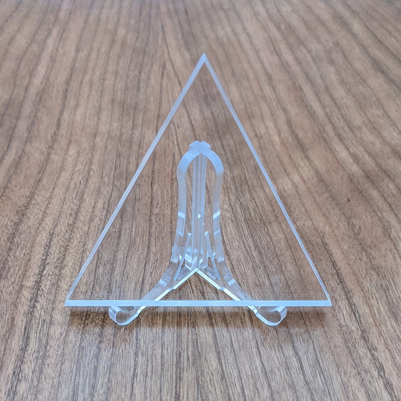 May include: A clear acrylic triangle display stand with a three-pronged base.