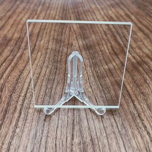 May include: A clear acrylic sheet on a clear plastic stand. The sheet is rectangular and has a smooth surface.