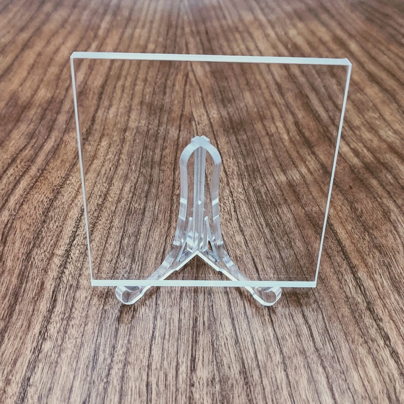May include: A clear acrylic sheet on a clear plastic stand. The sheet is rectangular and has a smooth surface.
