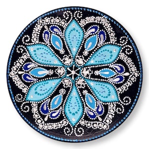 Könnte beinhalten: Ein schwarzer runder Teller mit einem blauen und weißen Mandala-Design, das darauf gemalt ist. Das Mandala zeigt eine zentrale Blume mit acht Blütenblättern, umgeben von einem sich wiederholenden Muster aus tropfenförmigen Formen.