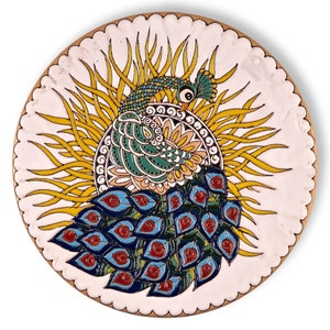 May include: A round ceramic plate with a hand-painted design of a peacock with a yellow sunburst behind it. The peacock's feathers are blue, green, and red.