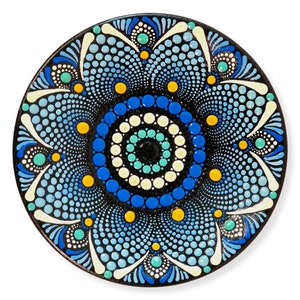 May include: A circular, black decorative plate with a mandala design. The mandala is made up of blue, light blue, white, yellow, and teal dots arranged in concentric circles and floral patterns. The plate has a glossy finish.