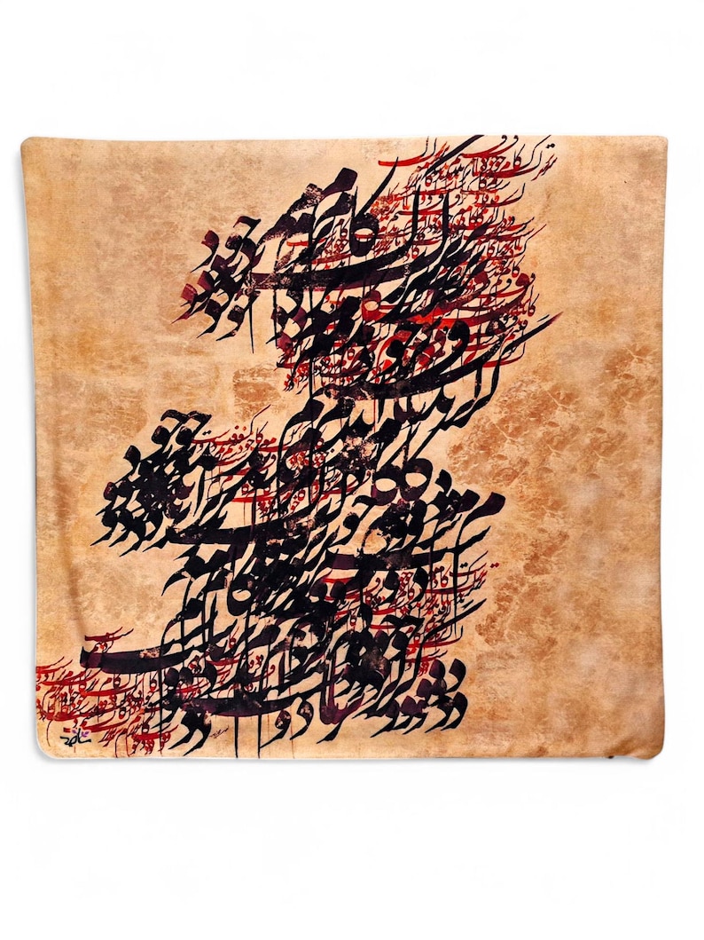May include: A square, tan-colored decorative pillow featuring intricate black and red calligraphy. The calligraphy is arranged in a flowing, artistic design across the pillow's surface. The pillow has a soft, textured appearance.