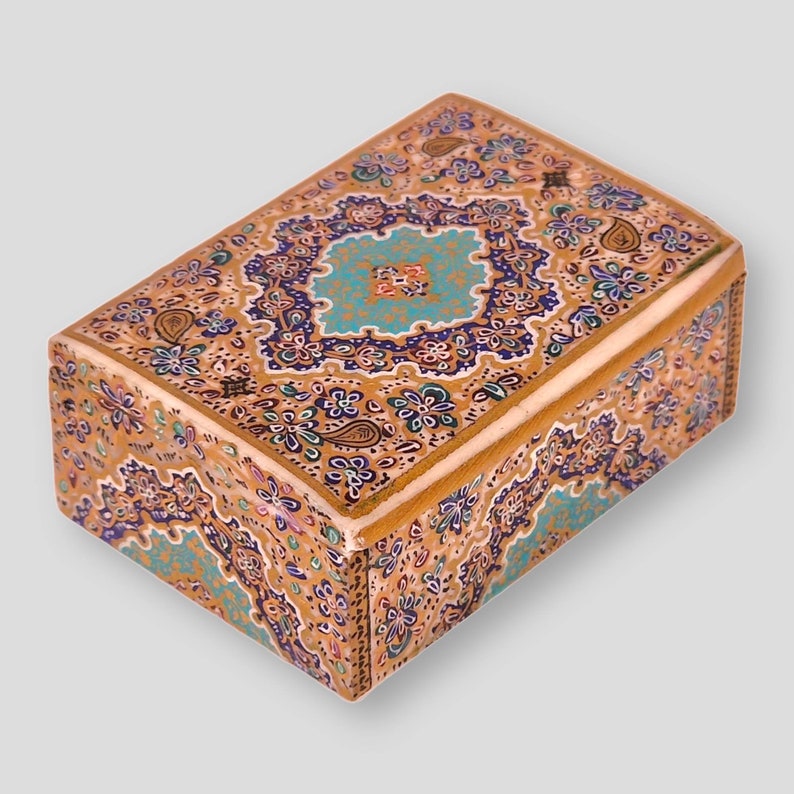 May include: A small wooden box with a decorative floral design in shades of blue, gold, and brown. The box is intricately painted with a paisley pattern.