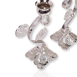 May include: A pair of silver menorah candle holders with a floral design. The candle holders are made of metal and have a delicate, intricate design.