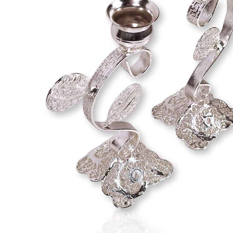 May include: A pair of silver menorah candle holders with a floral design. The candle holders are made of metal and have a delicate, intricate design.
