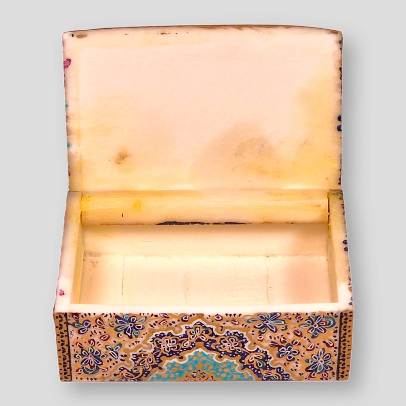 May include: A small, decorative box with a hinged lid. The box is made of wood and is painted with a colorful floral pattern. The inside of the box is lined with a soft, white material.