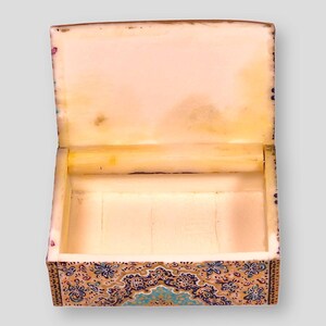May include: An open, intricately decorated box with a white interior. The box is made of wood and has a floral pattern in shades of blue, gold, and brown.