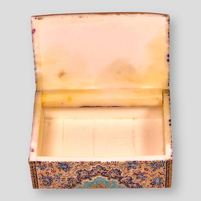 May include: An open, intricately decorated box with a white interior. The box is made of wood and has a floral pattern in shades of blue, gold, and brown.