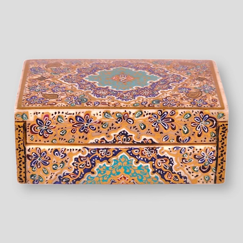 May include: A decorative wooden box with a hinged lid. The box is painted with intricate floral patterns in shades of gold, blue, green, and white.