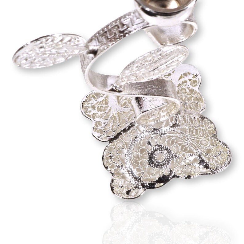 May include: A silver filigree ring with a delicate floral design. The ring is intricately crafted with a swirling pattern and a small round opening at the top.