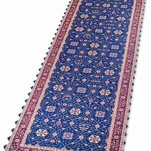 May include: A long, narrow blue rug with a red and white border. The rug has a floral pattern and a scalloped edge.