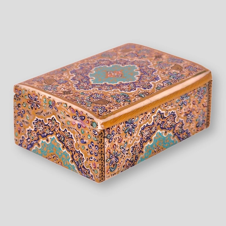 May include: A small wooden box with a hinged lid, decorated with intricate floral patterns in shades of blue, gold, and green. The box is made of wood and has a polished finish.
