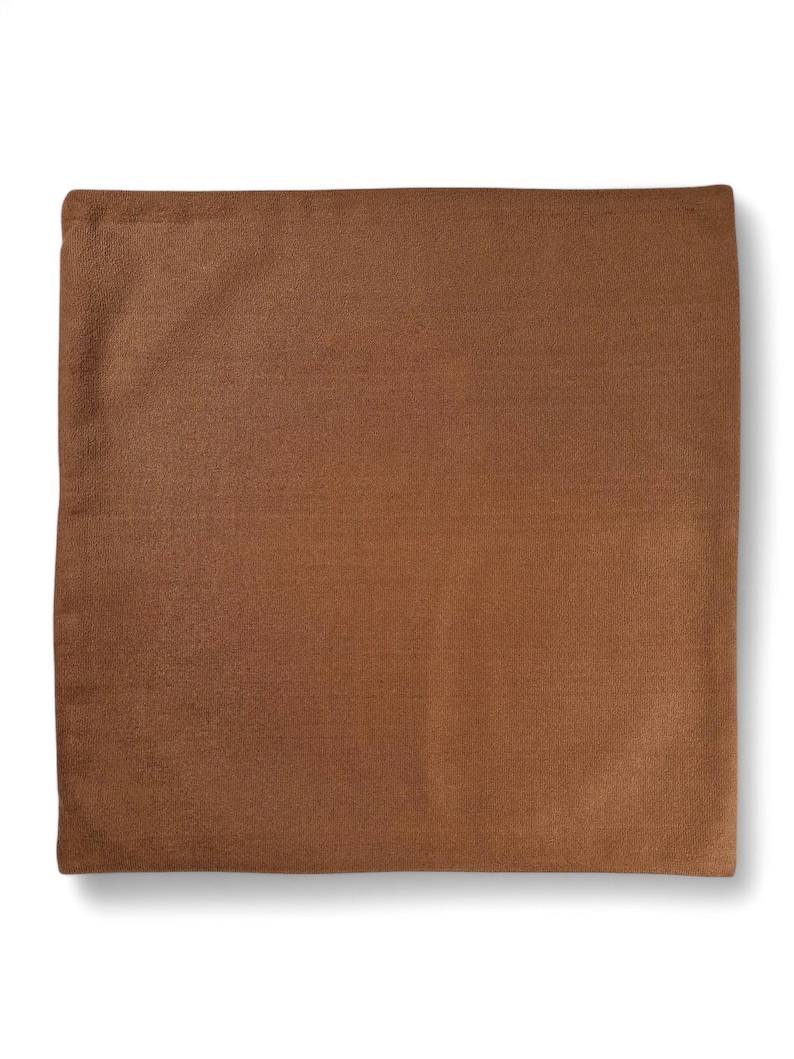 May include: A square, brown pillow cover with a textured surface. The pillow cover is a solid color and appears to be made of a soft fabric. The pillow cover is likely for home decor.