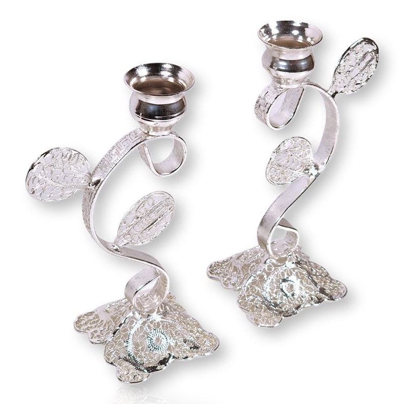 May include: A pair of silver candlestick holders with a delicate, floral design. The holders are made of filigree metal and have a swirling, vine-like shape. Each holder has a round base and a cup for holding a candle.