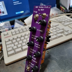 May include: A purple electronic music module with knobs and a jack. The module is labeled "555 Techno Kick" and "By NEWY". The knobs are labeled "Trigg", "Dec", "Freq", "Pulse Widt", "Note Tone", "Note Vol", "Pop Tone", and "Pop Vol".