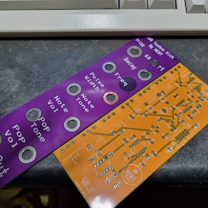 May include: A purple and orange circuit board with knobs and text that reads "55 Techno Kick", "Trigg", "By NEWY", "ssort", "Decay", "Freq", "Pulse", "Width", "Note", "Tone", "Note", "Vol", "Pop", "Tone", "Pop", "Vol", and "Out".