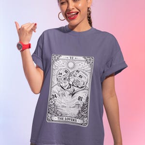 May include: A periwinkle t-shirt featuring a black and white illustration of two hockey players kissing, with the text "THE LOVERS" at the bottom. The shirt is a soft, comfortable material.
