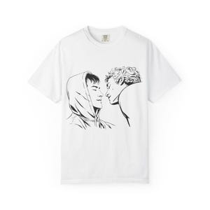 May include: White t-shirt with a black and white line drawing of two figures in an intimate pose. One figure wears a hoodie, the other leans in. The graphic is centrally placed on the tee.