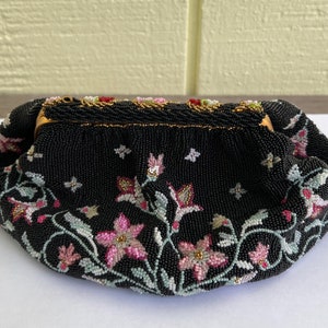 May include: A black beaded evening bag featuring a floral design. The bag is embellished with pink, white, and green beads, creating a delicate and intricate pattern.
