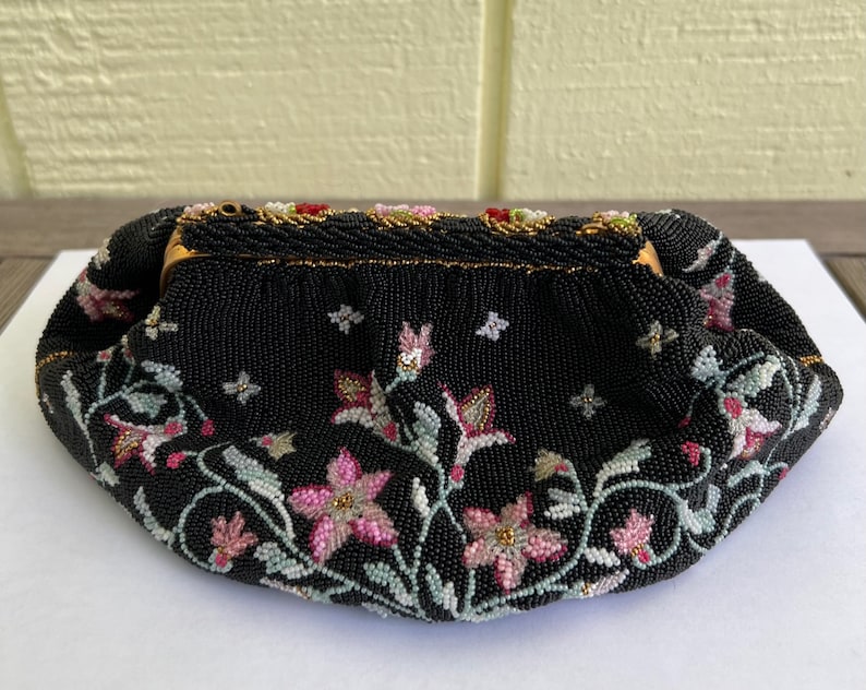 May include: A black beaded evening bag featuring a floral design. The bag is embellished with pink, white, and green beads, creating a delicate and intricate pattern.
