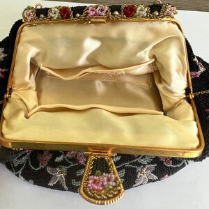 May include: A black beaded evening bag with a floral design and a gold clasp. The bag is lined with a cream-coloured fabric.